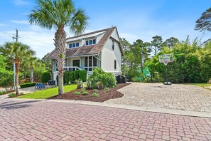 A two-story house with a large front yard, a basketball hoop, and a driveway.