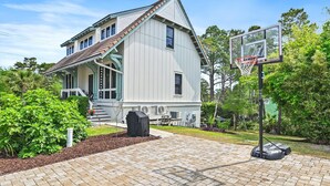 Ett hus med en basketkorg, en grillplats under tak och en välskött trädgård.