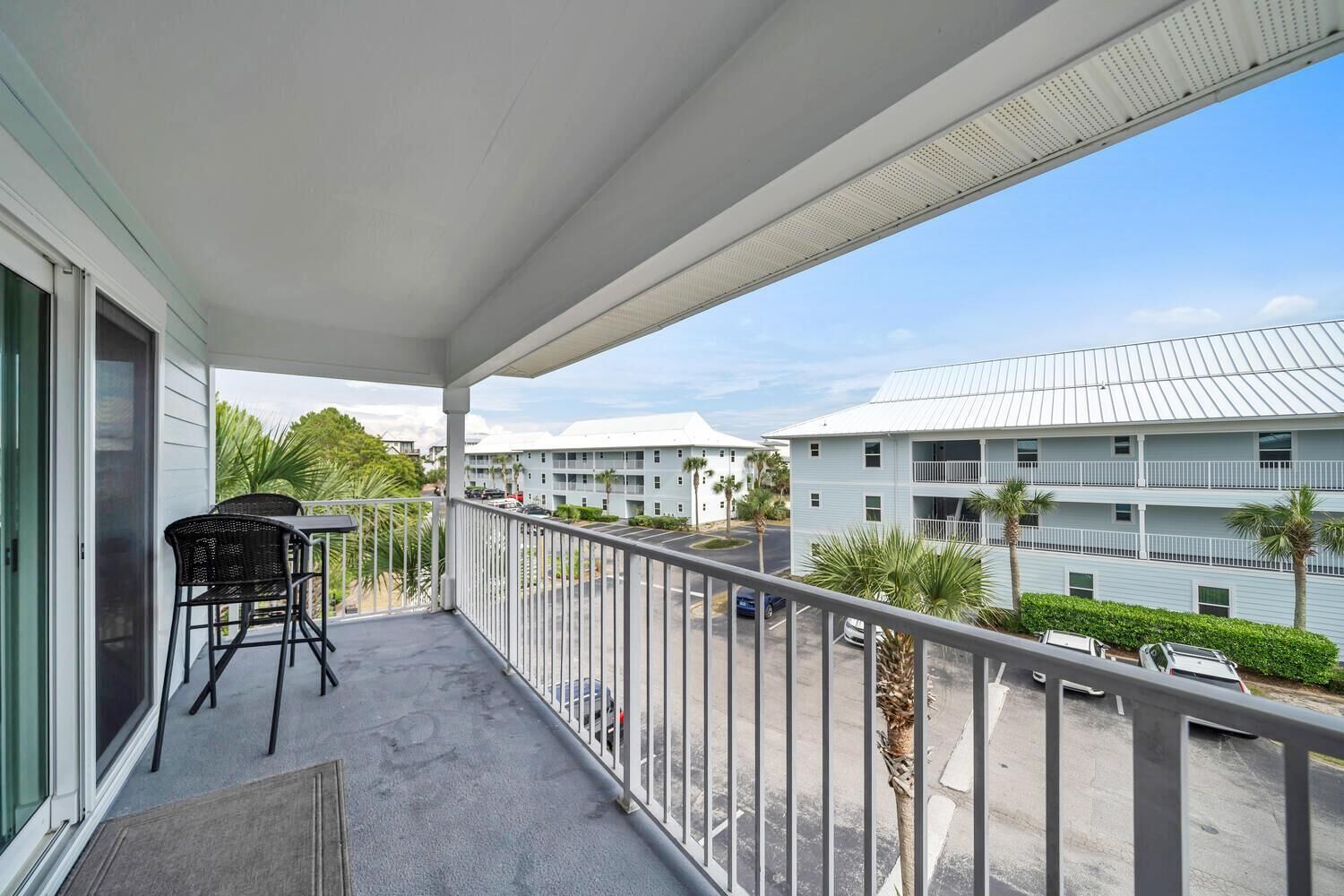 A balcony with a table and chairs, overlooking a parking area and a row of buildings.