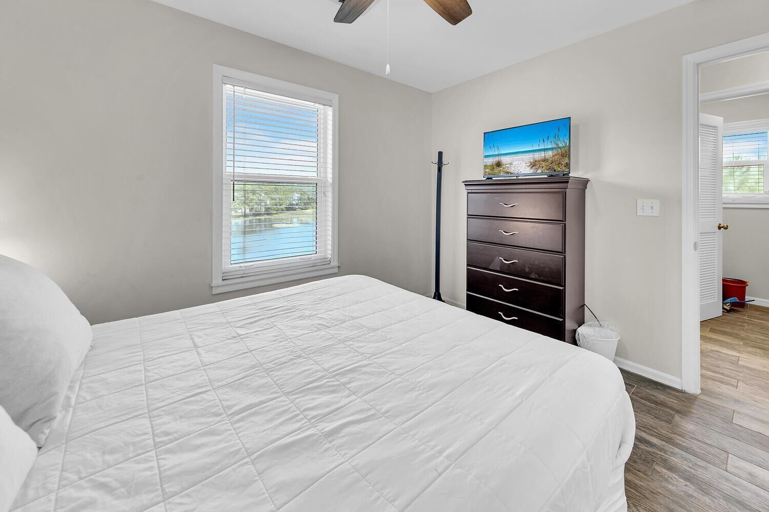 A bedroom with a bed, a dresser, a window with blinds, and a painting on the wall.