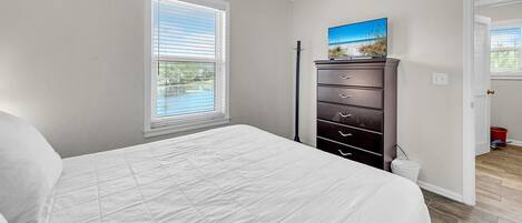 A bedroom with a bed, a dresser, a window with blinds, and a painting on the wall.