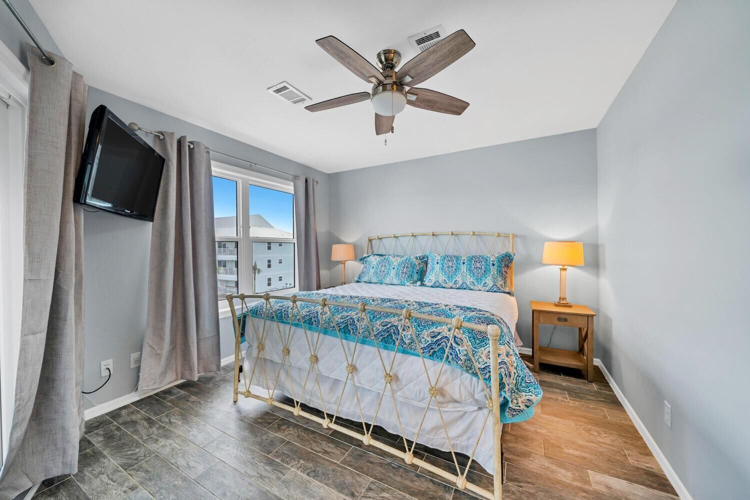 Une chambre à coucher avec un lit, un ventilateur de plafond, une télévision et une fenêtre avec des rideaux.