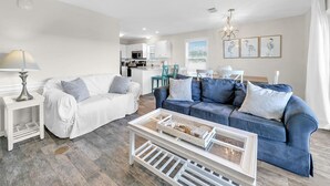 A modern living room with a white sofa, a blue sofa, and a coffee table. There is a kitchen in the background. - Beachside Villas 933 (Santa Rosa Beach)