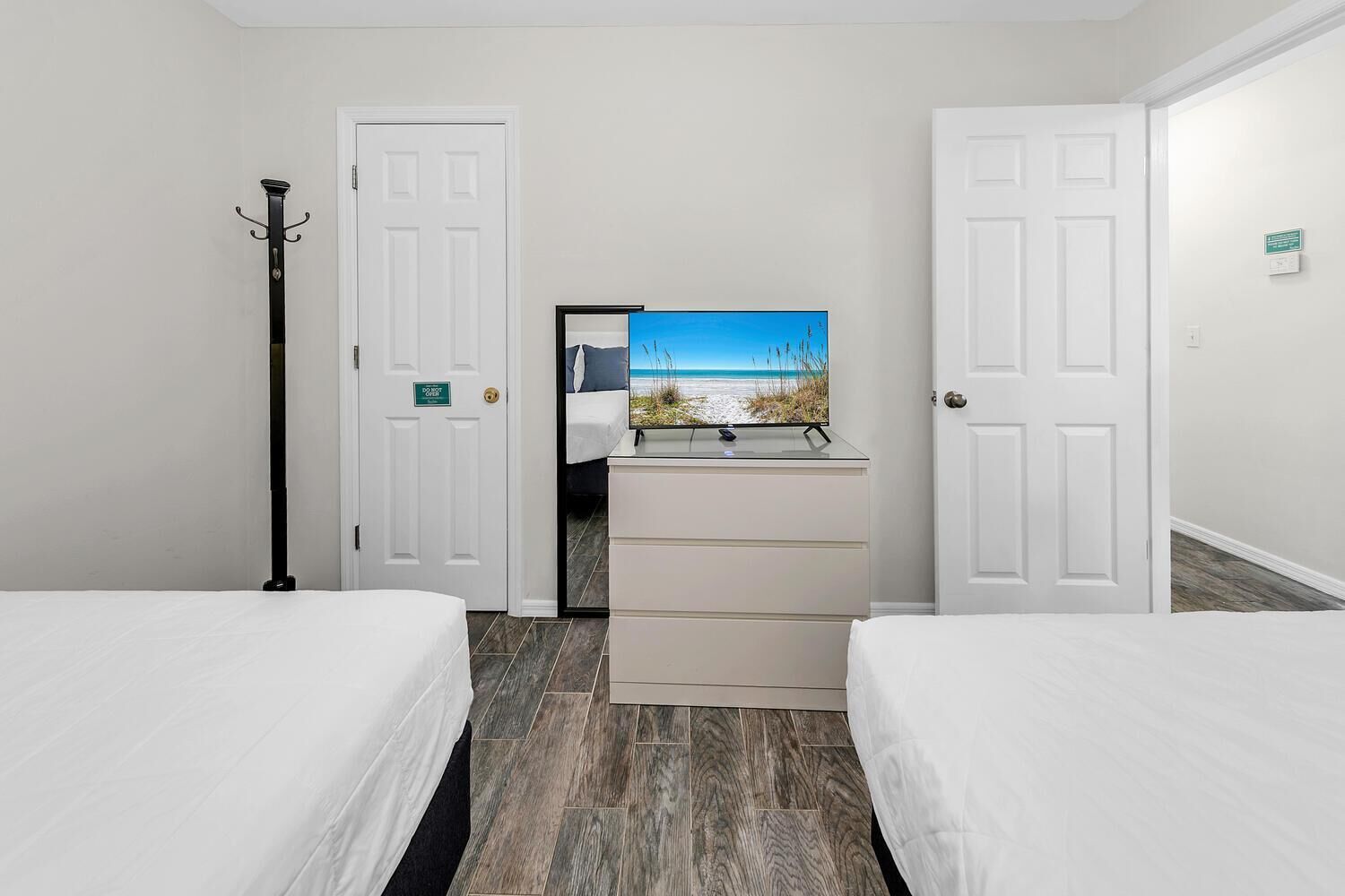 A hotel room with two beds, a dresser, a coat rack, and a painting of a beach scene.