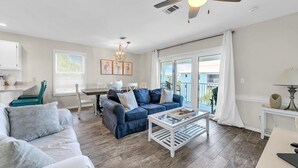 A living room with a sofa, a coffee table, and a dining area with a table and chairs. - Beachside Villas 933 (Santa Rosa Beach)