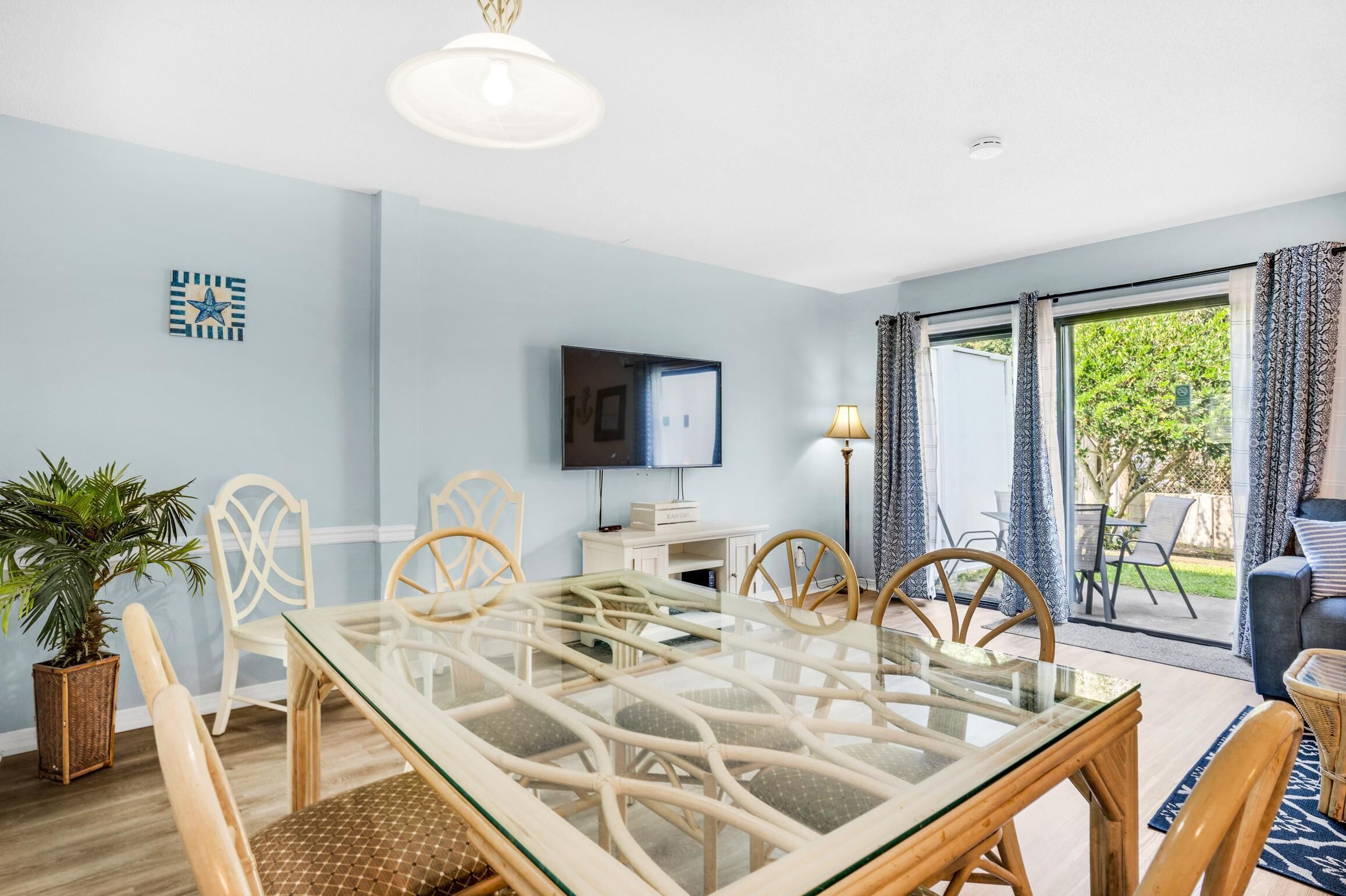 Un coin repas avec une table à plateau en verre, des chaises en osier, une plante en pot et un téléviseur posé sur un meuble.
