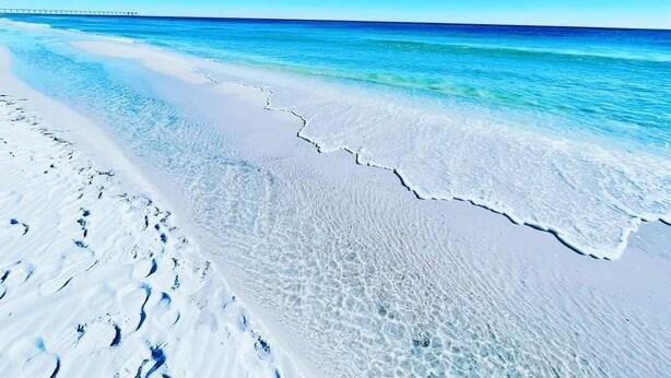 Une plage à l’eau d’un bleu cristallin, avec une jetée qui s’étend au loin.