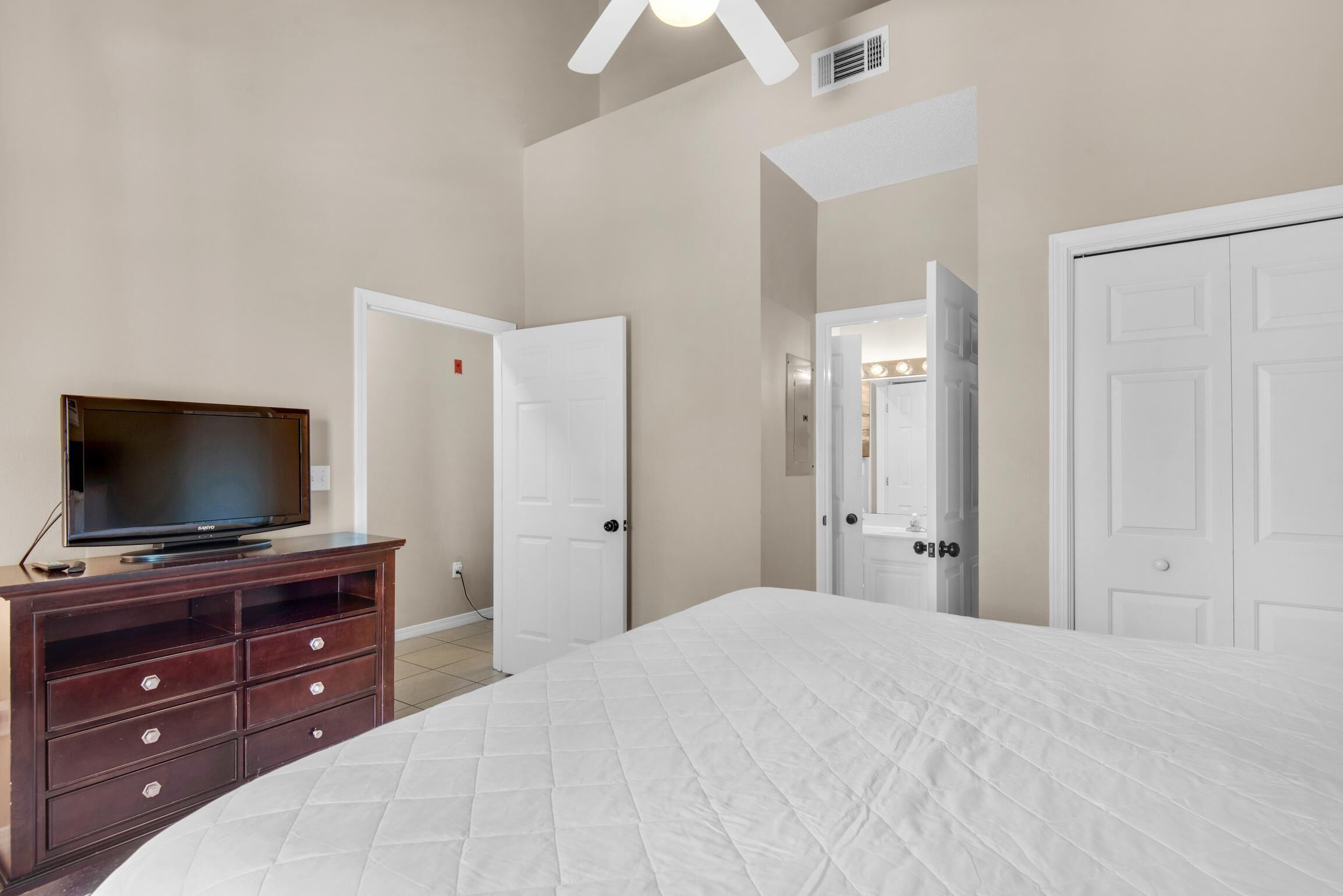 Une chambre à coucher avec un lit, un téléviseur posé sur une commode en bois et des portes blanches.