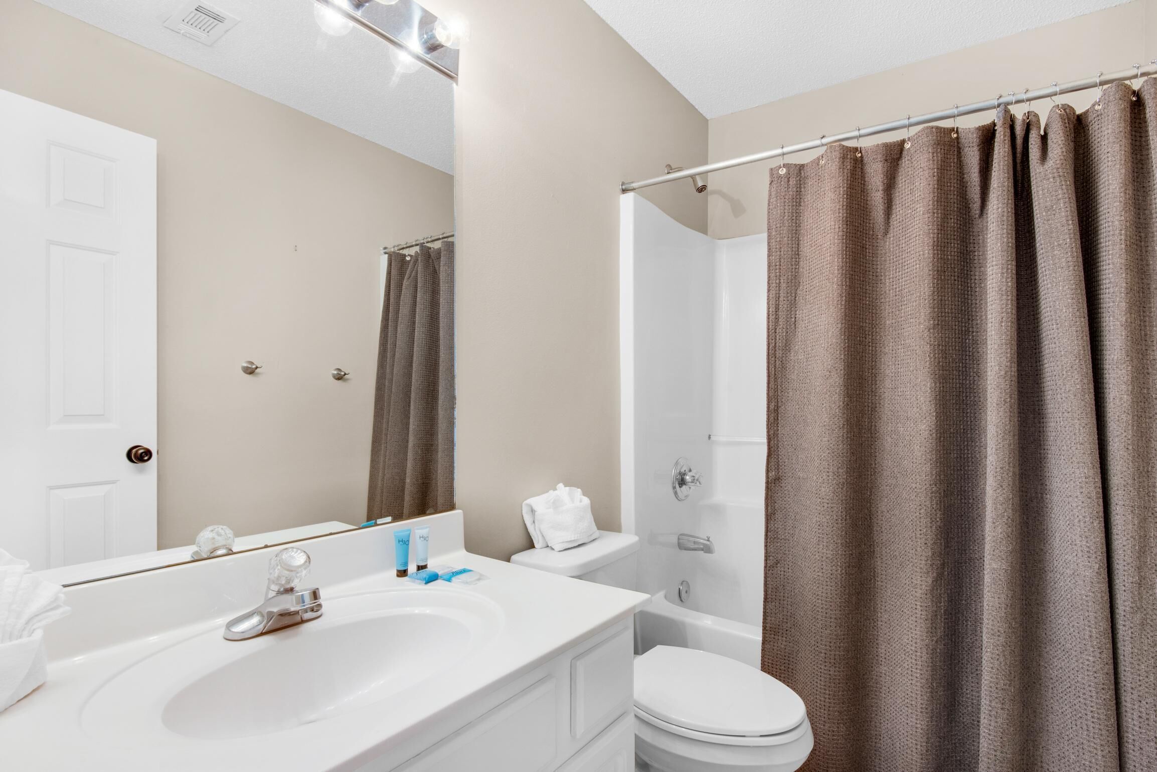 A bathroom with a white sink, mirror, and toilet, a shower curtain, and a towel rack.