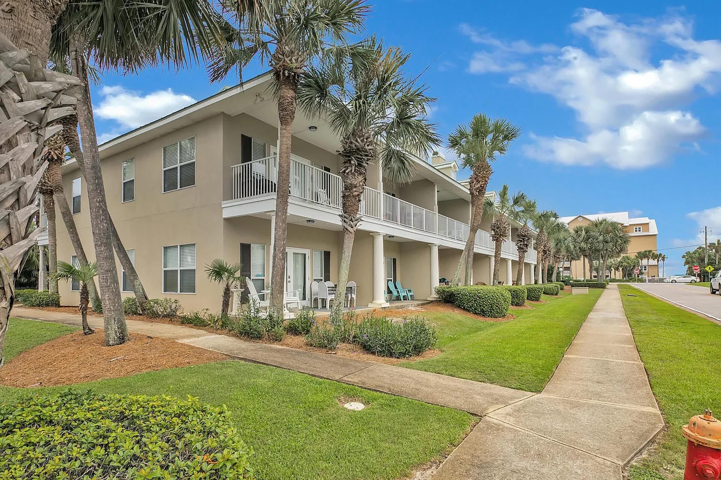 A multi-story hotel with balconies, palm trees, and a well-maintained lawn.