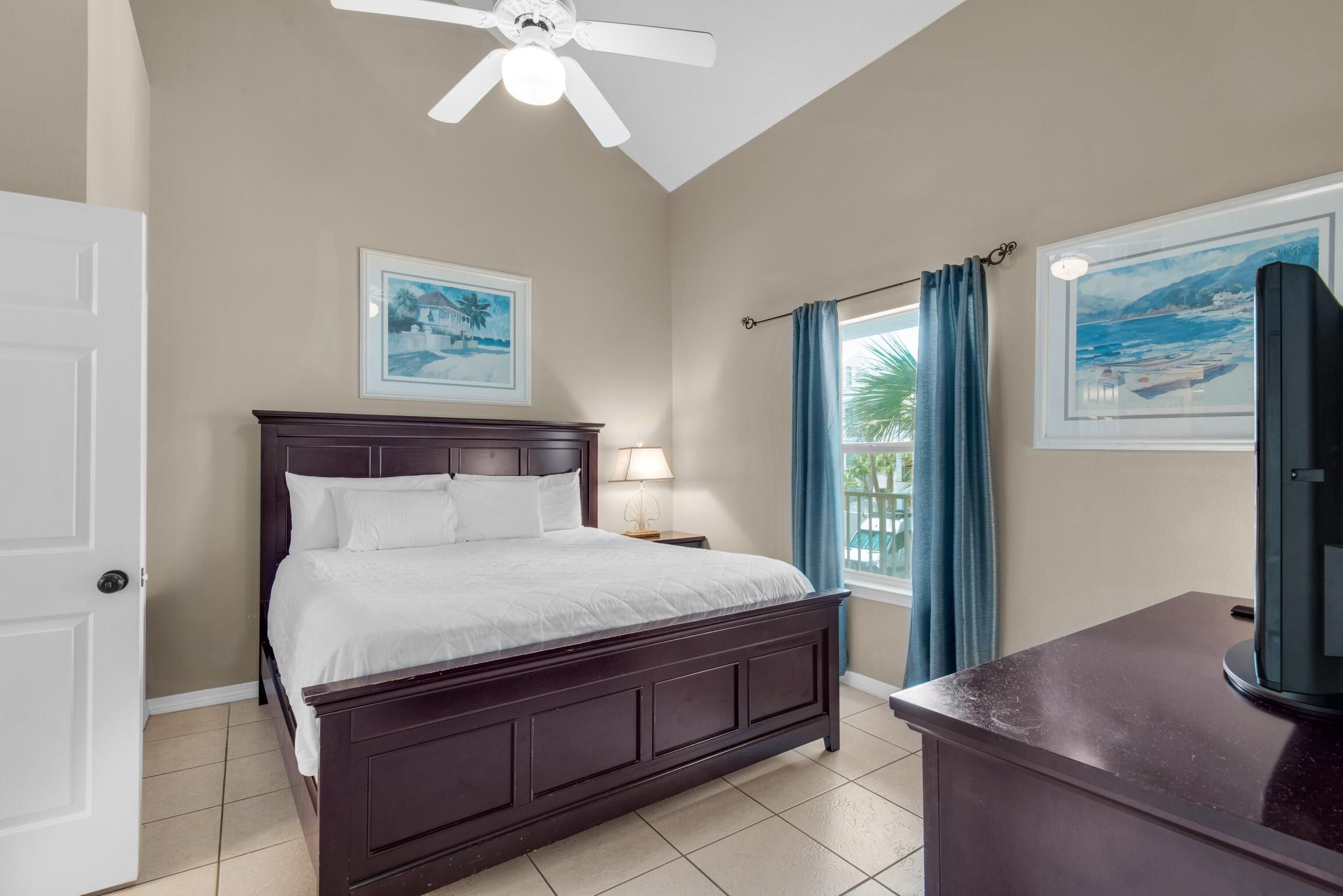 A bedroom with a bed, a nightstand, a ceiling fan, a window with curtains, and a TV.