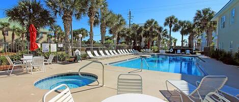A pool area with lounge chairs and a small table, surrounded by palm trees and a building in the background.