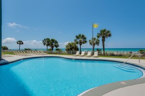 A swimming pool with lounge chairs and palm trees, overlooking a beach. - Long Beach Resort 1-904 (Panama City Beach)