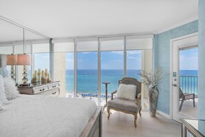A bedroom with a large bed, a dresser, a chair, a vase, and a balcony with a view of the beach and ocean. - Long Beach Resort 1-904 (Panama City Beach)