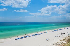 Une plage aux eaux turquoise et limpides, un rivage sablonneux et plusieurs parasols bleus.