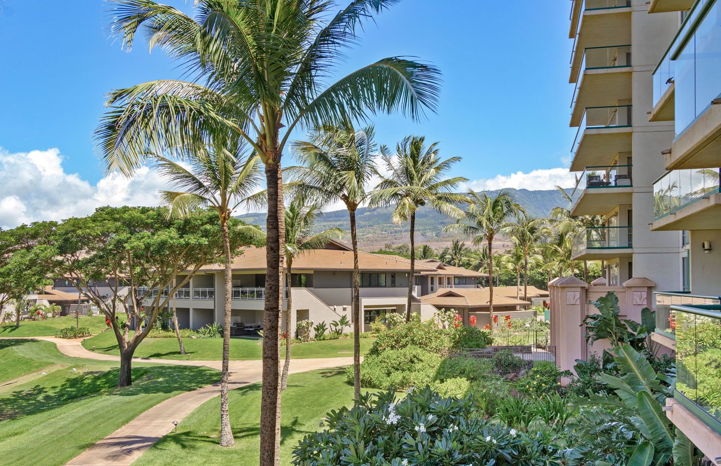 Un hotel con edificios de varios pisos, un jardín bien cuidado con palmeras y una vista despejada de montañas al fondo.