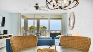 A dining area with a round table, wicker chairs, and a woven basket. - Magnolia House #202 (Destin)