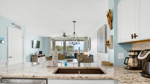 A kitchen with a granite countertop, stainless steel appliances, and a view to the outside. - Magnolia House #202 (Destin)