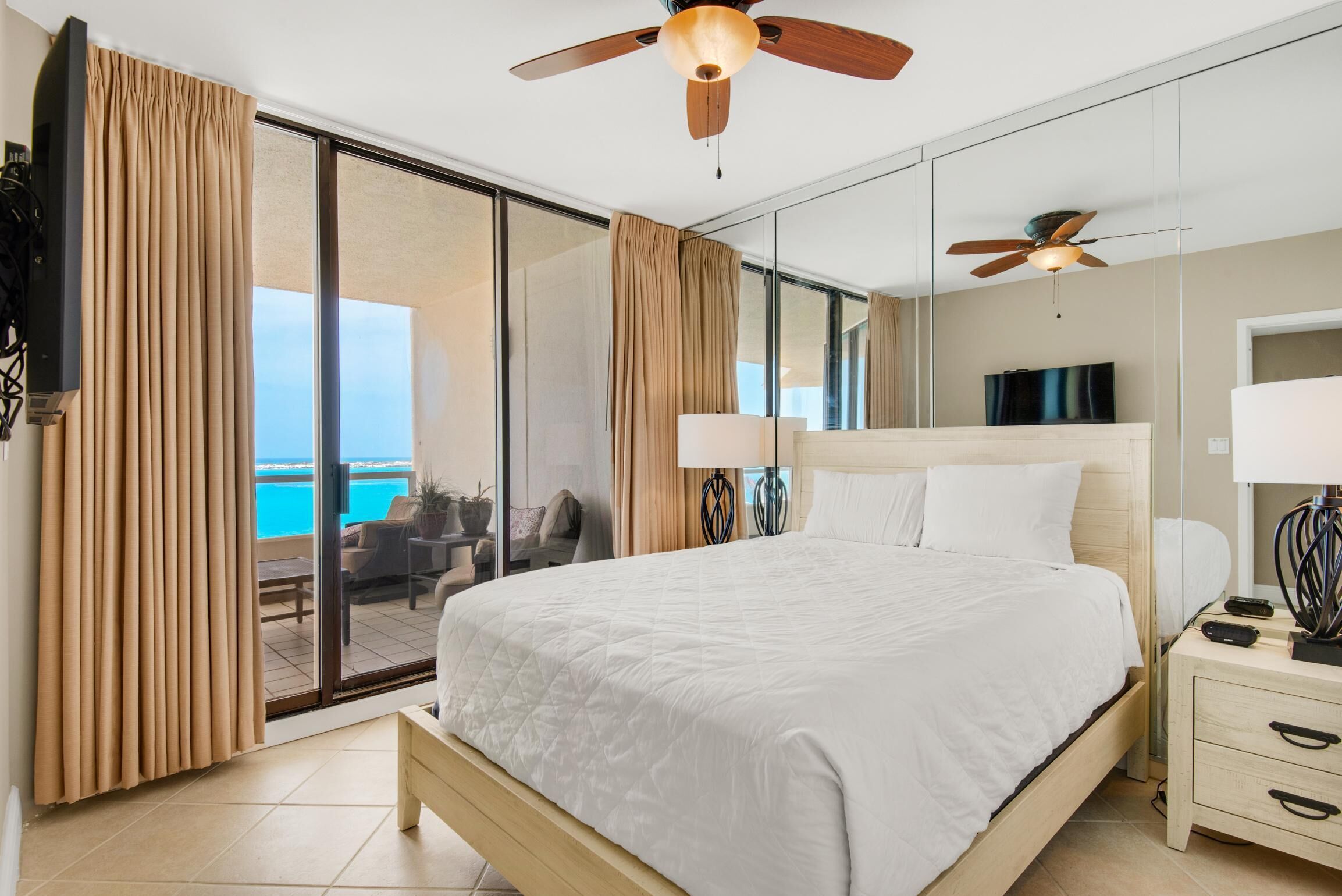 Hotelkamer met een groot bed, een plafondventilator, een nachtkastje en uitzicht op de oceaan door een schuifdeur.