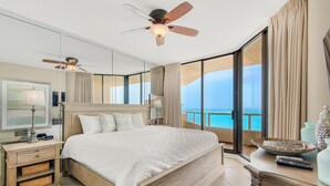 A spacious bedroom with a large bed, a ceiling fan, a nightstand, and a view of the ocean through large windows. - East Pass 309 (Destin)
