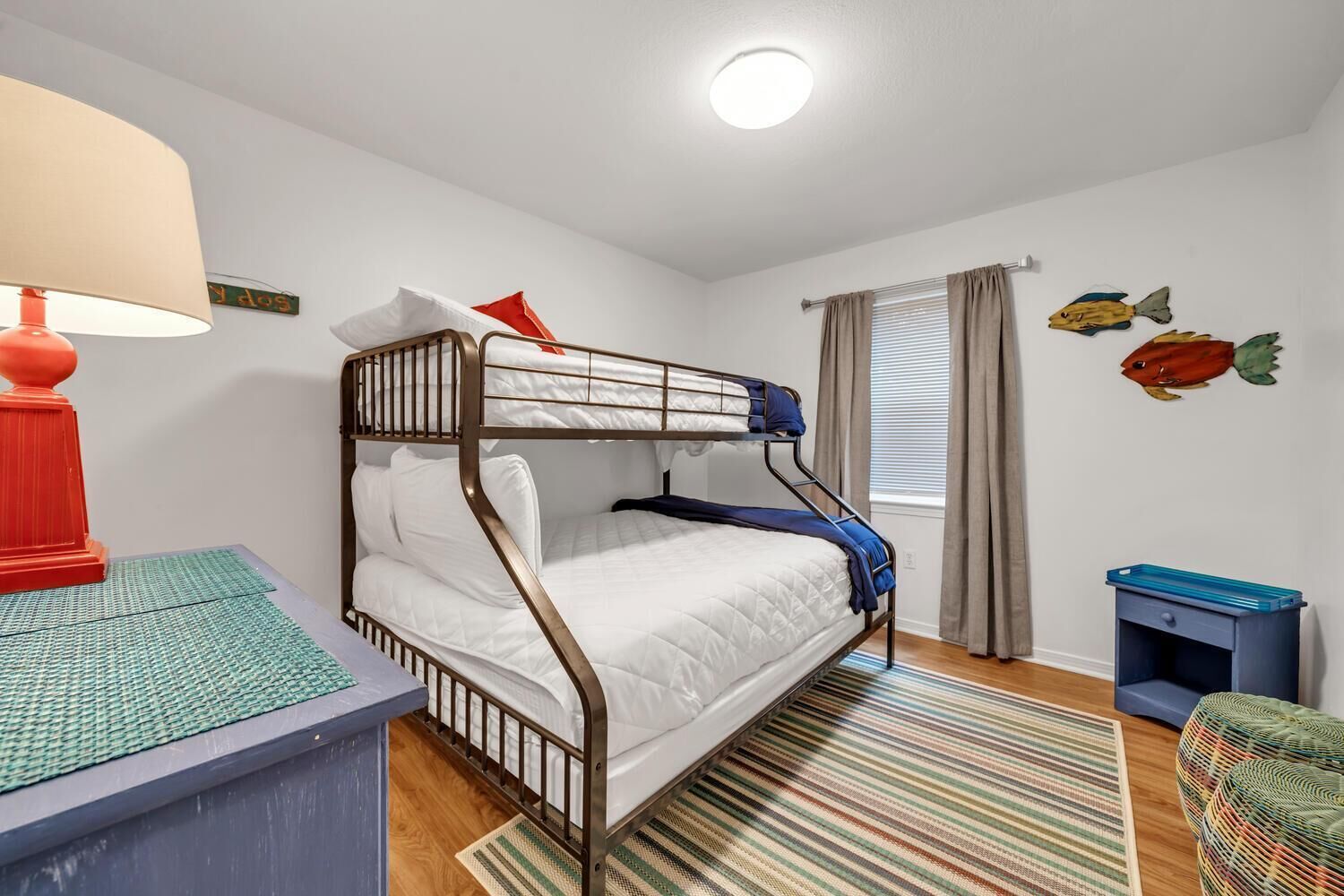A bunk bed room with a red lamp, a striped rug, and wall art.
