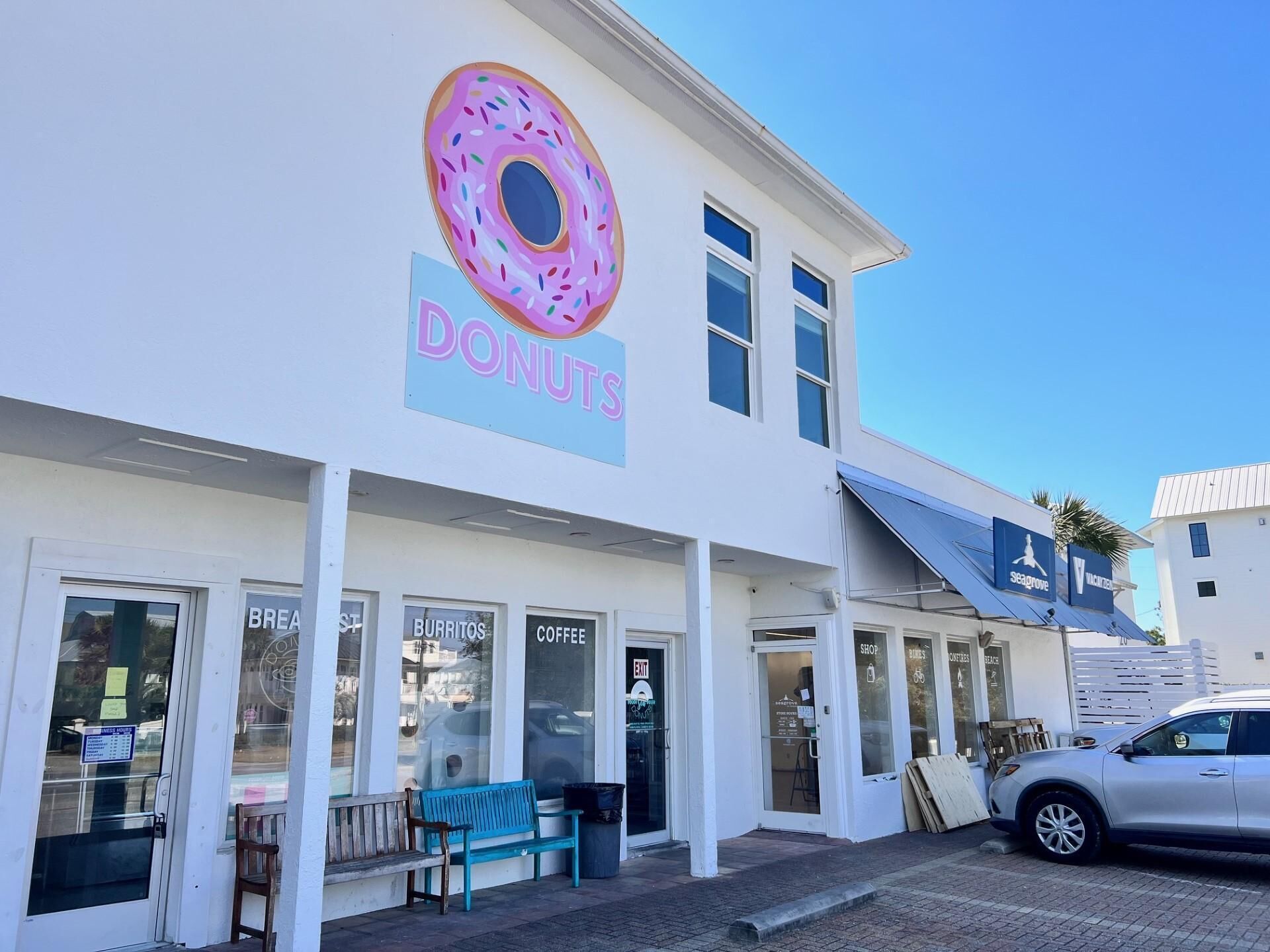 A building with a large donut sign, storefronts for 'Burritos' and 'Coffee', and a bench outside.