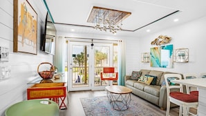 A modern living room with a sofa, dining table, and chairs. There is a large window with a view of the outdoors. - Summer Breeze 203 (Miramar Beach)