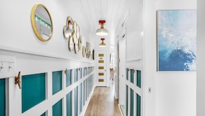 A hallway with teal and white paneling, gold-framed mirrors, and a blue abstract painting on the wall. - Summer Breeze 203 (Miramar Beach)