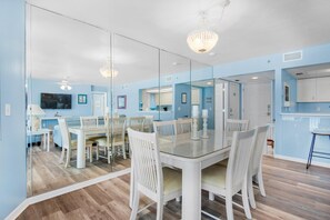 A modern dining area with a glass table, white chairs, and a chandelier.