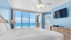 Une chambre avec un grand lit, un ventilateur de plafond, une télévision, une commode et une vue sur l’océan.