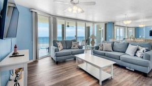 Un salon moderne avec un canapé gris, une table basse blanche et une grande fenêtre donnant sur la mer.