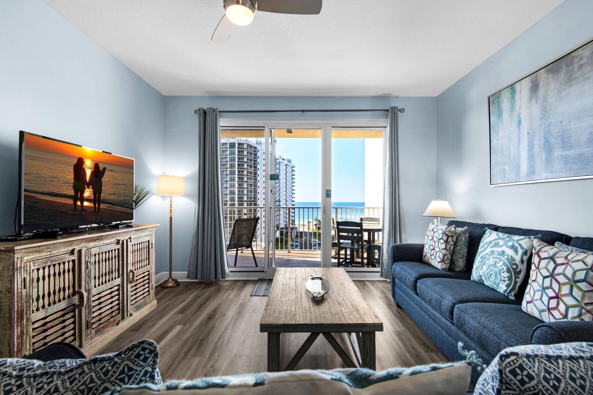 A living room with a television, a sofa, a coffee table, and a balcony with a view of the city.