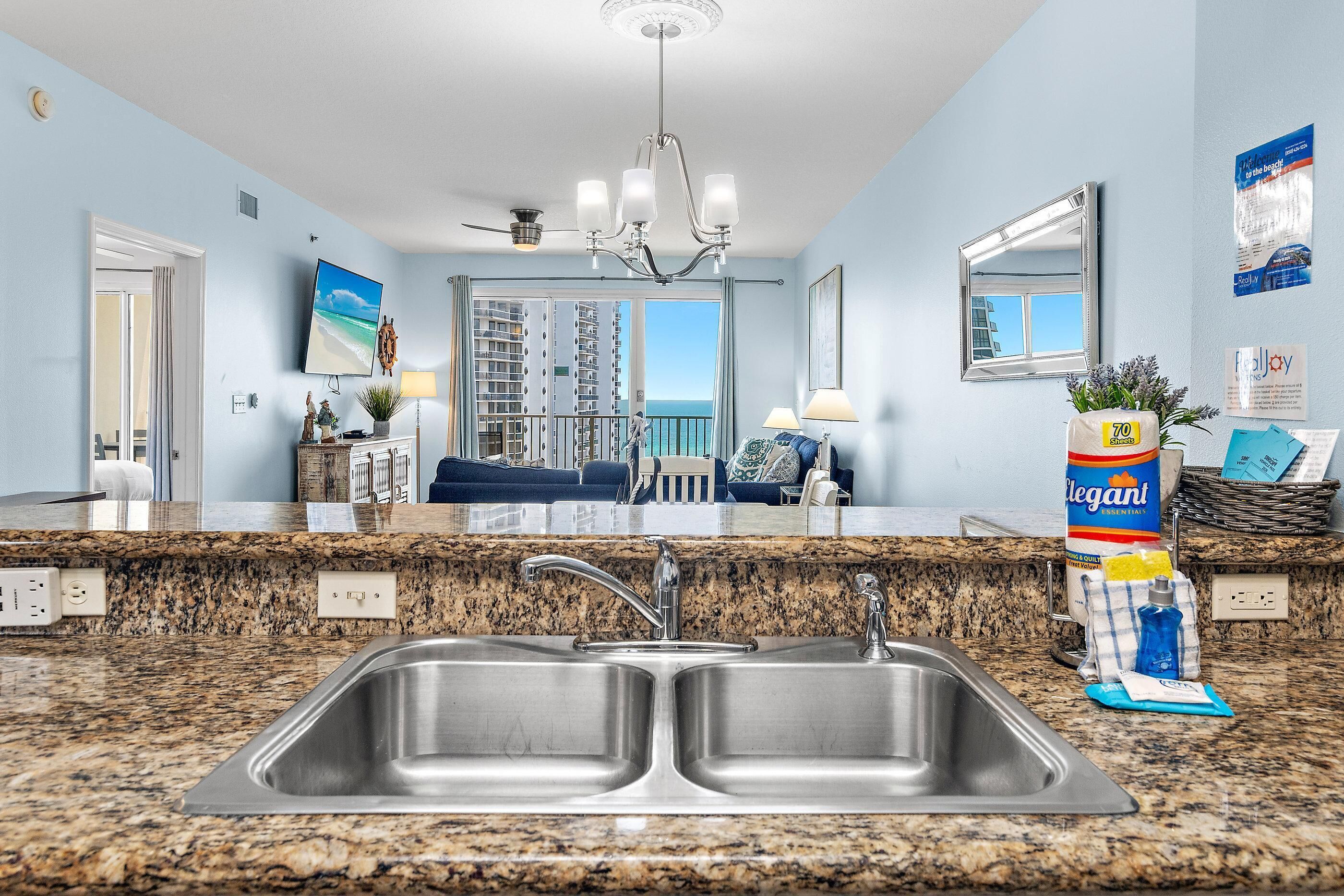 A hotel room with a large window, a double sink, a chandelier, and a view of the ocean.