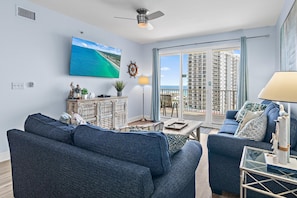 A living room with a large window, a ceiling fan, a mounted TV, and a view of a high-rise building. - Ariel Dunes I 803 (Miramar Beach)
