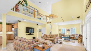 A spacious living area with a high ceiling, a balcony with decorative railings, and a kitchen area with wooden cabinets.