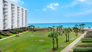 A hotel with a beachfront view, featuring a central courtyard with palm trees and a pool, and a building with multiple balconies. - Mainsail 227 (Miramar Beach)