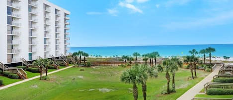Un hotel con vista a la playa, que cuenta con un patio central con palmeras y una piscina, además de un edificio con varios balcones.