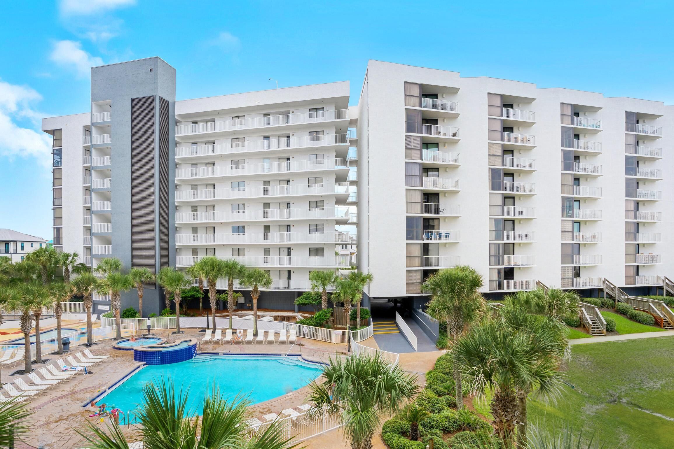 A modern hotel with multiple floors, a swimming pool, and palm trees.