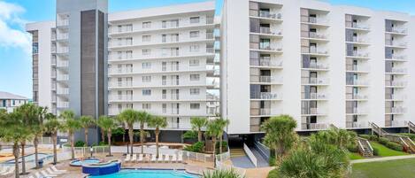 A modern hotel with multiple floors, a swimming pool, and palm trees.