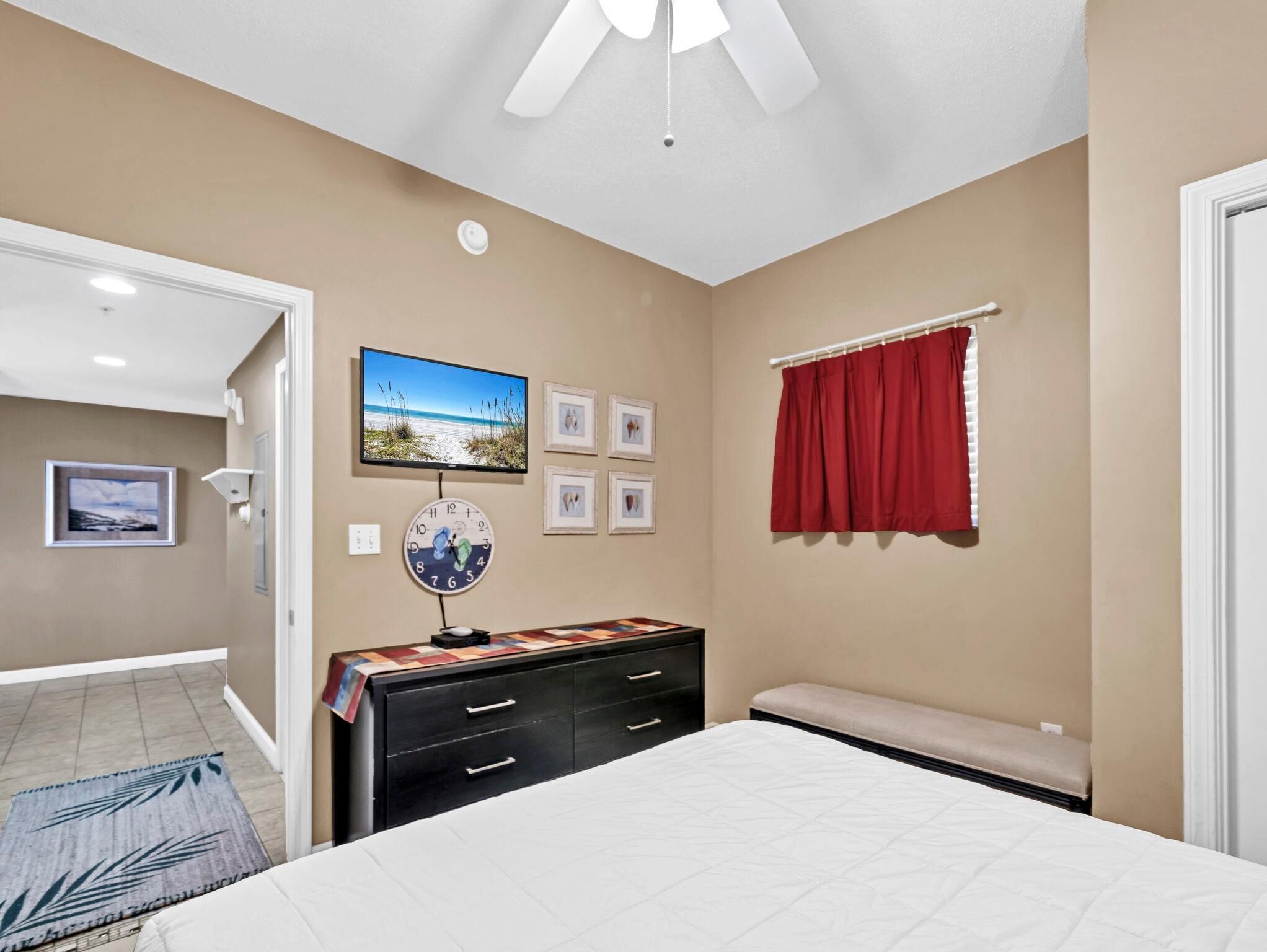 A bedroom with a bed, a dresser, a TV, and a window with red curtains.