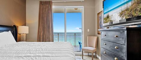 A hotel room with a bed, a dresser, a television, and a view of the ocean through a sliding door.