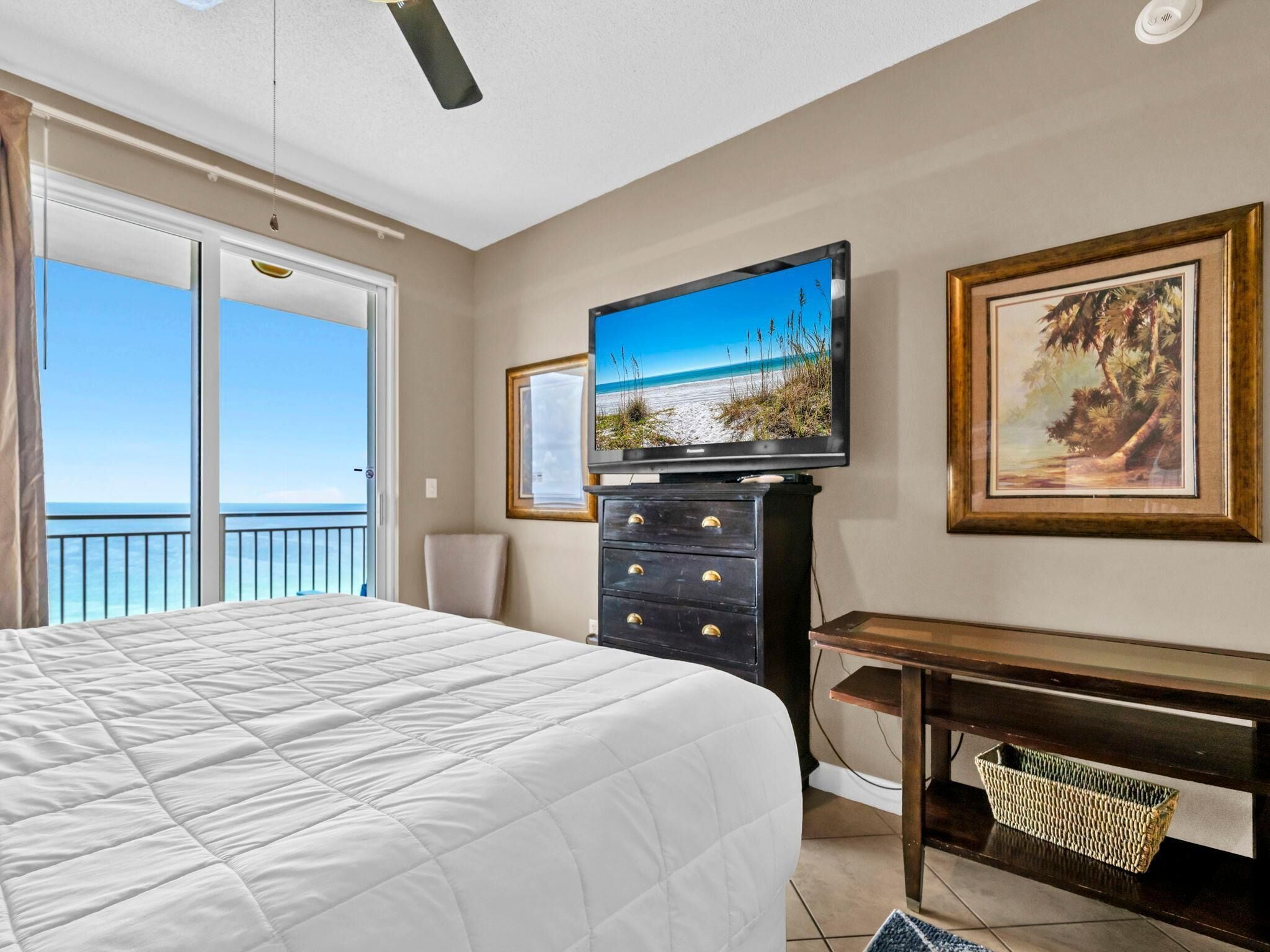 Habitación de hotel con cama, televisor, escritorio y ventana grande con vista a la playa.