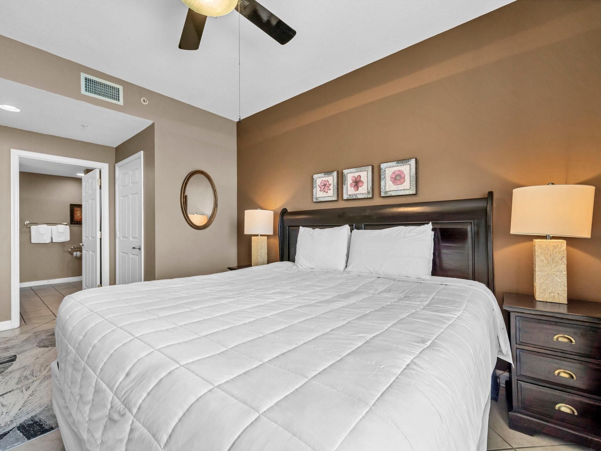 A hotel room with a large bed, two bedside tables, a ceiling fan, and a wall-mounted mirror.