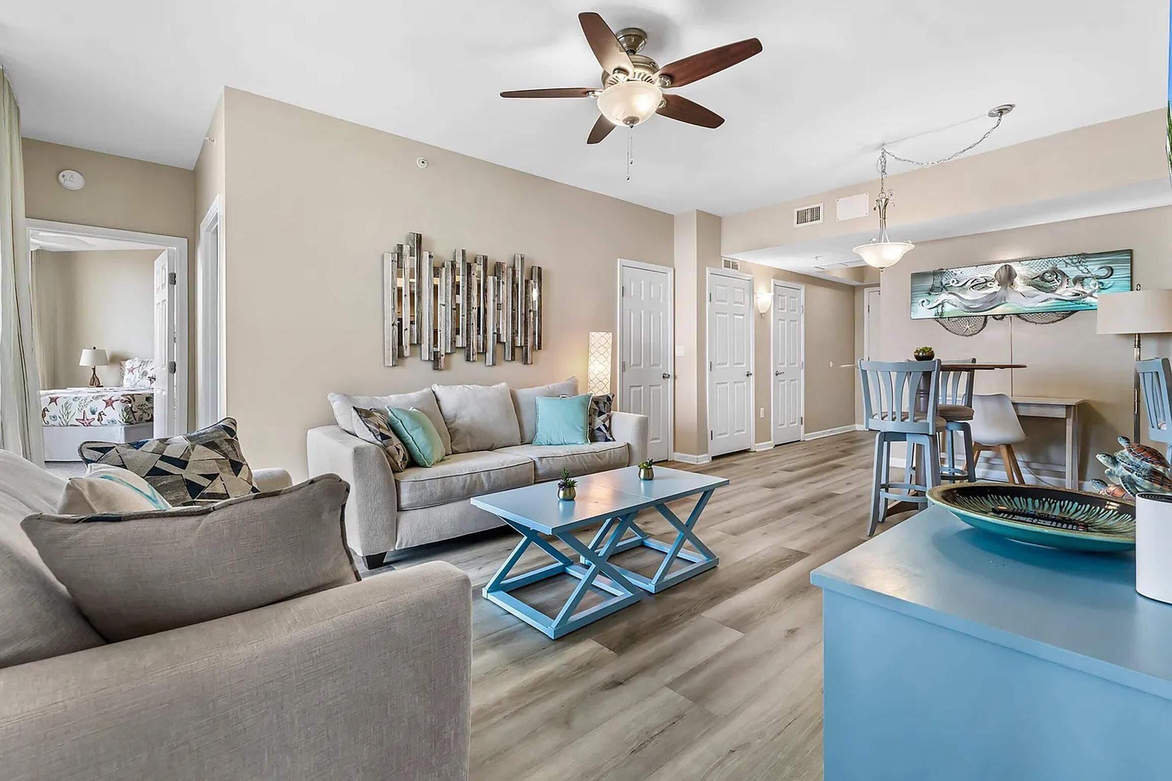A spacious living room with a beige sofa, a blue coffee table, and a dining area with a table and chairs.