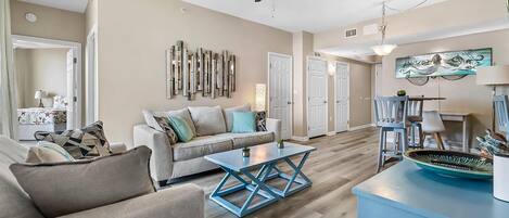 A spacious living room with a beige sofa, a blue coffee table, and a dining area with a table and chairs.