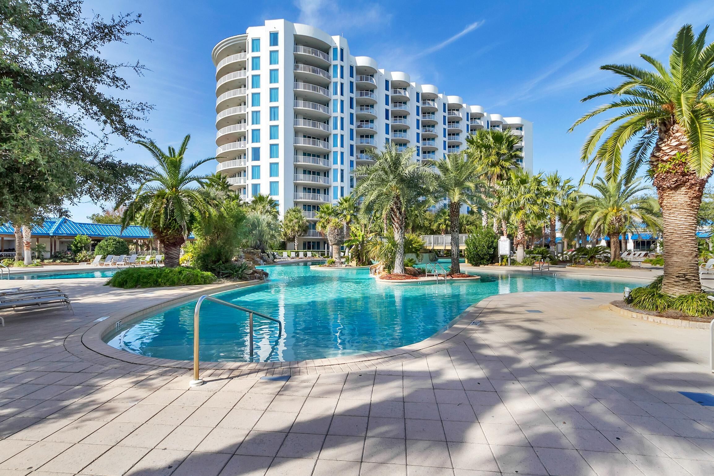Un hotel con una grande area piscina, palme e un edificio moderno con balconi.