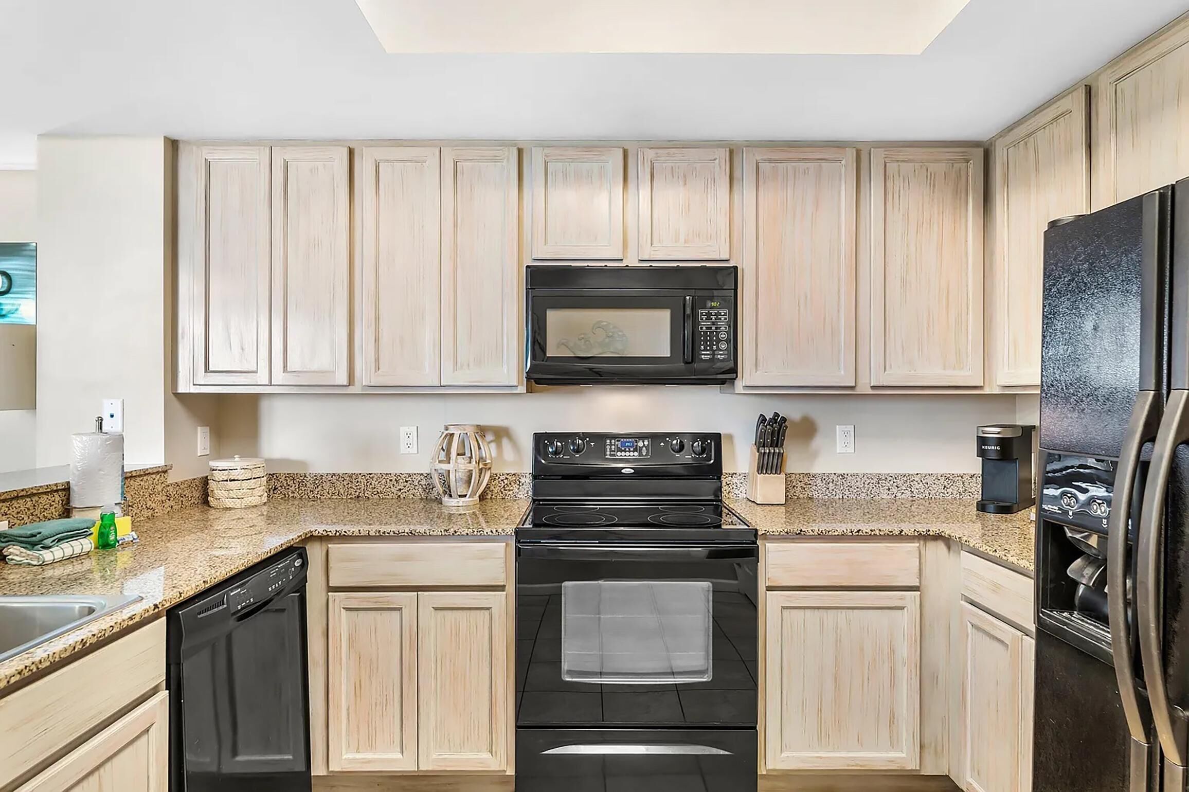 Una cocina con armarios de madera clara, un microondas negro, una estufa y un refrigerador.
