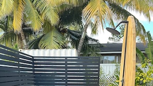 A small outdoor shower area with a black metal partition, a small round stool, and a hose attached to a wooden post. - Beach House,2 minutes walking to the beach and Restaurant The Beach House by 604 (Waianae)