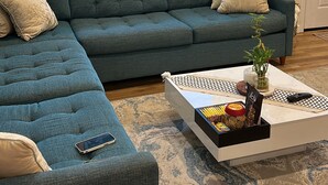 A living room with a sectional sofa, a coffee table with decorative items, a guitar, and a view of greenery through a window. - Beach House,2 minutes walking to the beach and Restaurant The Beach House by 604 (Waianae)