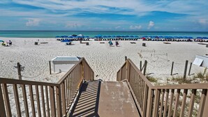 A beach with a wooden staircase leading down to the sand, blue umbrellas, and beach chairs. - Boardwalk 209 (Panama City Beach)